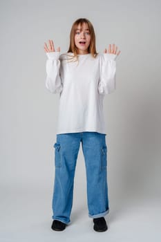 A surprised child wearing a white long-sleeve shirt and blue jeans expresses confusion in a studio setting close up