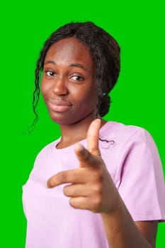 Young woman in a pink shirt playfully pointing fingers at the camera against a bright green background in studio