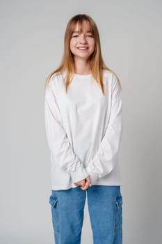 Young woman with long hair in a white sweatshirt standing against a light gray background close up