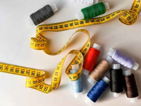 Colorful spools of thread and yellow measuring tape for sewing crafts.