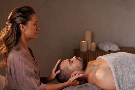 girl massage therapist gives head massage to man in office with warm light, pain in head and neck, healthy massaging rehab concept