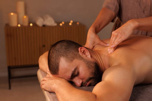 Relaxing neck massage, healthy massaging rehab concept. Close-up hands of woman masseur doing wellness medical relaxing massage for male patient in dark medical office in shadow. Copy ad text space