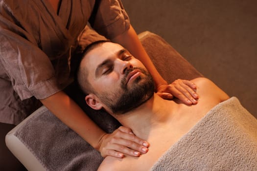 girl masseuse massages man's chest in warm atmosphere of spa salon, relaxing wellness massage for patient