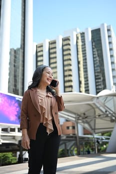 Portrait of confident mature businesswoman talking on cell phone with modern buildings behind.