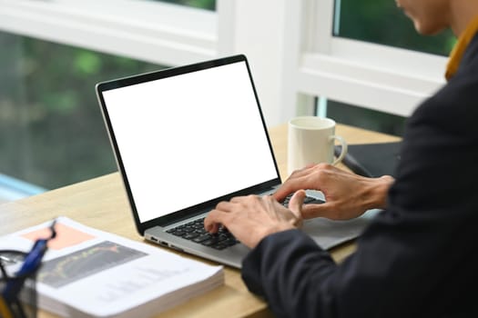 Businessman in suit working on laptop with blank screen for mockup.
