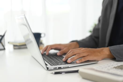 Close up of businessman typing on keyboard in modern workspace.
