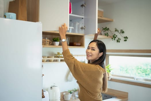 Smiling young woman organizing kitchen cabinet in cozy home.