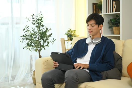 Handsome young asian man using digital tablet on a sofa at home.