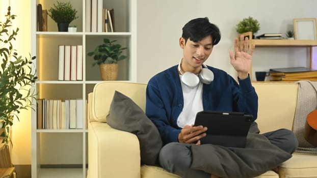 Friendly asian man having an online video chat on digital tablet at home.