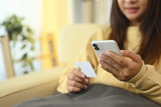 Cropped short happy young woman making online transaction at home with mobile application.