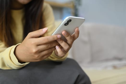 Young woman typing text message on mobile phone and relaxing on couch at home.