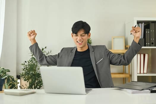 Excited young entrepreneur celebrating positive business results at workplace.