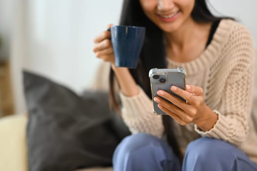 Happy young woman sipping coffee and checking message on her mobile phone.
