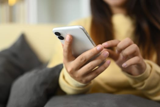 Young woman typing text message on mobile phone and relaxing on couch at home.