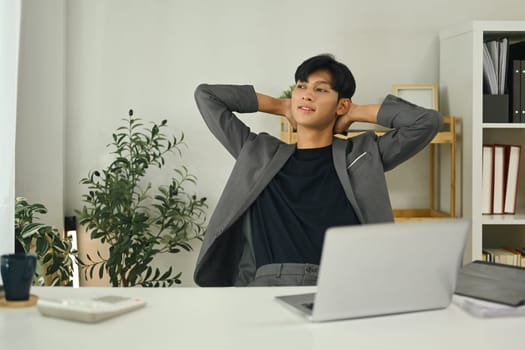 Businessman leaning back in office chair relaxing with hands behind head.
