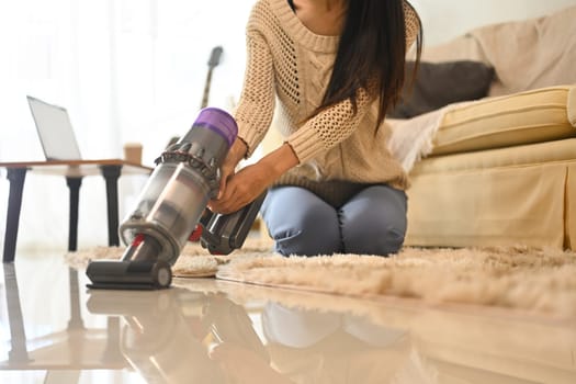 Close up of unrecognizable woman vacuuming floor with a cordless vacuum cleaner.