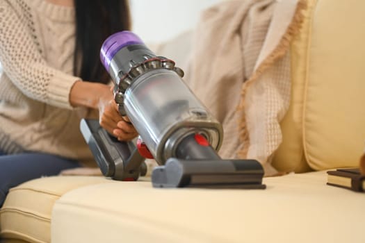 Young woman vacuuming couch surface with cordless vacuum.