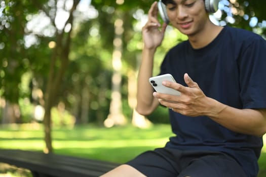 Smiling young sports man resting after training outdoors and using mobile phone.
