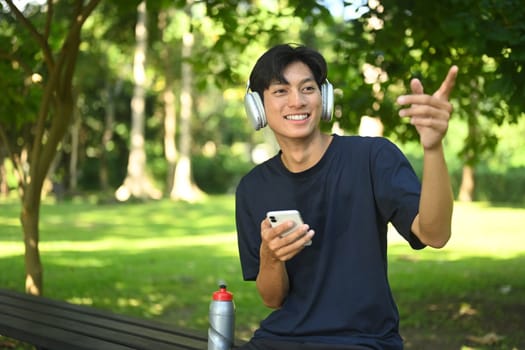 Smiling young sports man resting after training outdoors and using mobile phone.