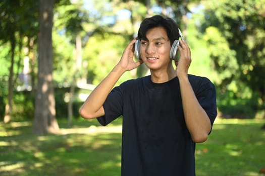 Handsome male runner listening to music on headphones and taking a break after jogging in the park.