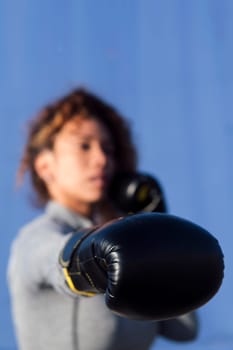 unrecognizable adult female boxer ready to fight on boxing gloves during workout on blue background, concept of strength and healthy lifestyle, selective focus