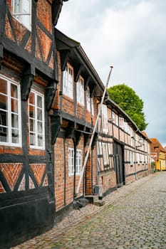 A picturesque view of traditional half-timbered houses lining an old cobblestone streetin ebeltoft in denmark, evoking a sense of history and European charm. The overcast sky adds a serene atmosphere.
