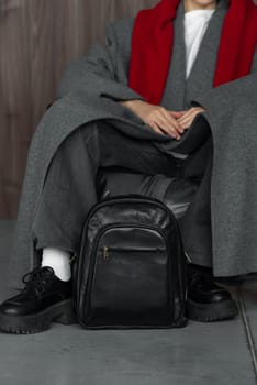 woman posing with a leather backpack wearing a warm gray coat and black shoes.