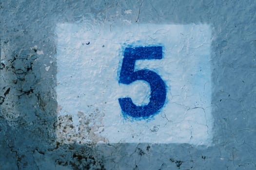 Number five painted on a blue mud-stained wall in a white rectangle. High quality photo
