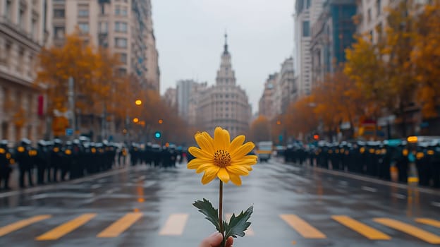 A close-up of a hand holding a yellow flower facing a police line in an urban street, symbolizing peace, hope, and resistance in a tense demonstration setting.
