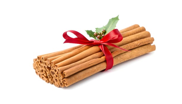 A neatly tied bundle of cinnamon sticks with a sprig of holly and a red ribbon, isolated to highlight its holiday warmth and coziness. Perfect for festive and winter themes