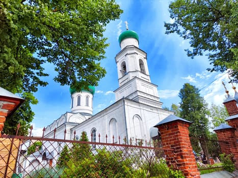 A serene church featuring green domes is nestled among lush trees, contrasting against a bright blue sky.