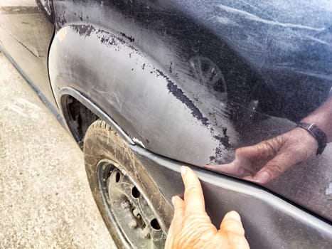 A person is seen pointing at a noticeable scratch on a black colored cars exterior, drawing attention to the damaged area