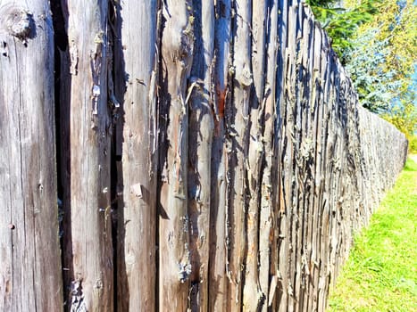 A weathered wooden fence stretches along a vibrant green field, highlighting the natural textures of the aged wood under bright sunlight.