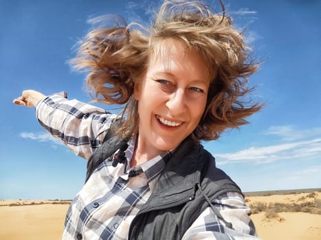 A blogger enjoys a lively moment in the desert, posing for a joyful selfie against the clear blue sky