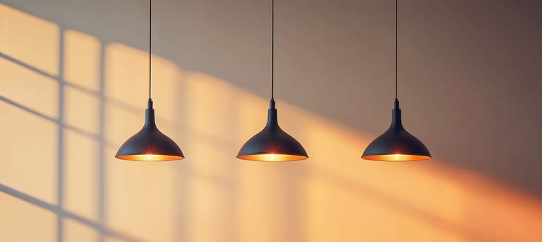 Three modern black and gold hanging lamps illuminate a room, casting a warm glow against a wall with a window shadow