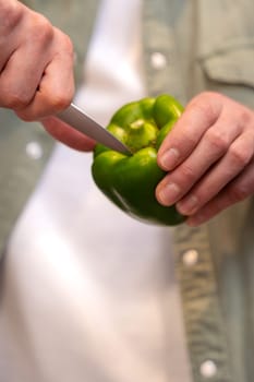 A close-up of a person slicing a fresh green bell pepper with a knife. The image highlights precision and care in food preparation, showcasing vibrant colors and the freshness of the vegetable.
