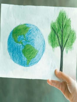 Child is holding a drawing of planet earth and a tree, symbolizing the importance of environmental protection for a sustainable future