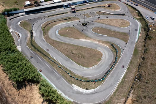 Drone capturing go-karts moving on winding race tracks from top aerial perspective. Distant view of racing competition on road at countryside during daytime.