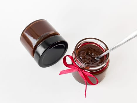Homemade chocolate spread in jar with red ribbon on white background.