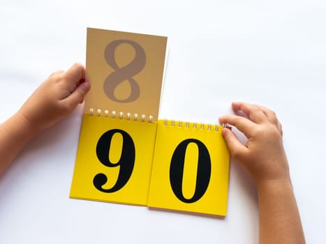 Childs hands flip through yellow pages with numbers. Displaying number 90 on white background.