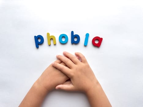 Childrens hands holding in anxiety concept with colorful phobia letters on white background.