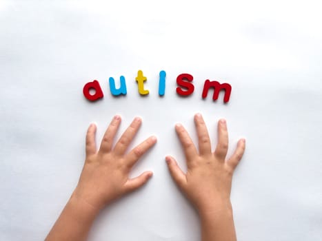 Childs hands and colorful letters spelling autism on white background.