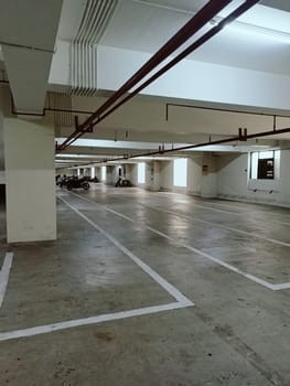Empty underground parking garage featuring concrete flooring and bright overhead lighting. Spacious area with marked parking lines, suitable for vehicles. Industrial setting with structural beams in view.
