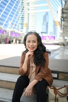 Confident mature businesswoman sitting on steps with a smile in the city center.