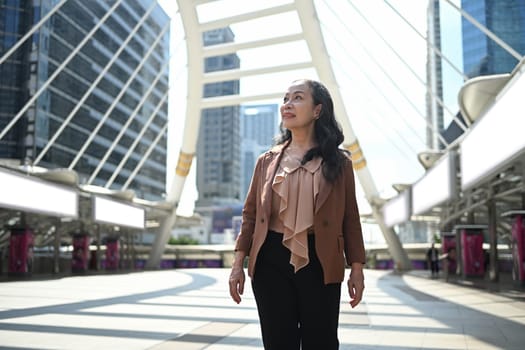 Elegant middle aged businesswoman in stylish suit walking through downtown.