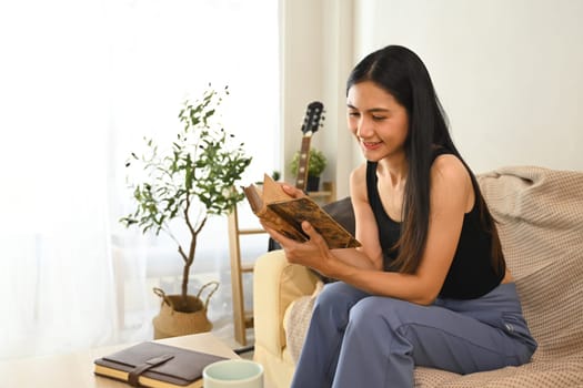 Beautiful young woman enjoys quiet time with a book in living room.