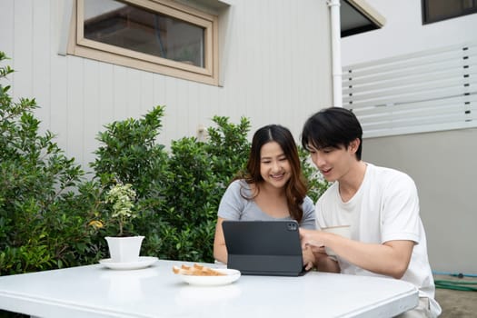 Happy asian couple sharing moments and using digital tablet in garden.