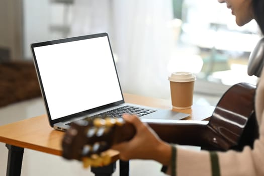 Cropped shot of young woman learning guitar through online lessons on laptop.