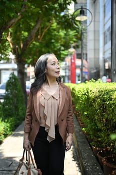 Positive mature businesswoman strolling through an urban park on beautiful day.