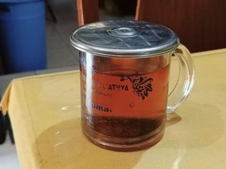 Warm glass of tea with a floral design on a clear mug with metal lid, placed on a wooden table. Perfect for cozy moments and relaxation. Captures a traditional tea-drinking experience.